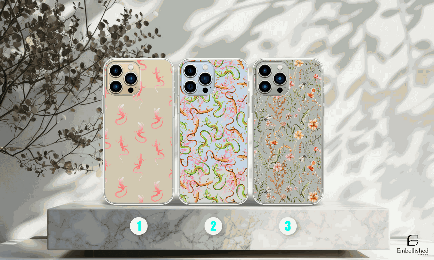 Clear phone cases with vibrant lizard and floral wild flower designs on a marble platform