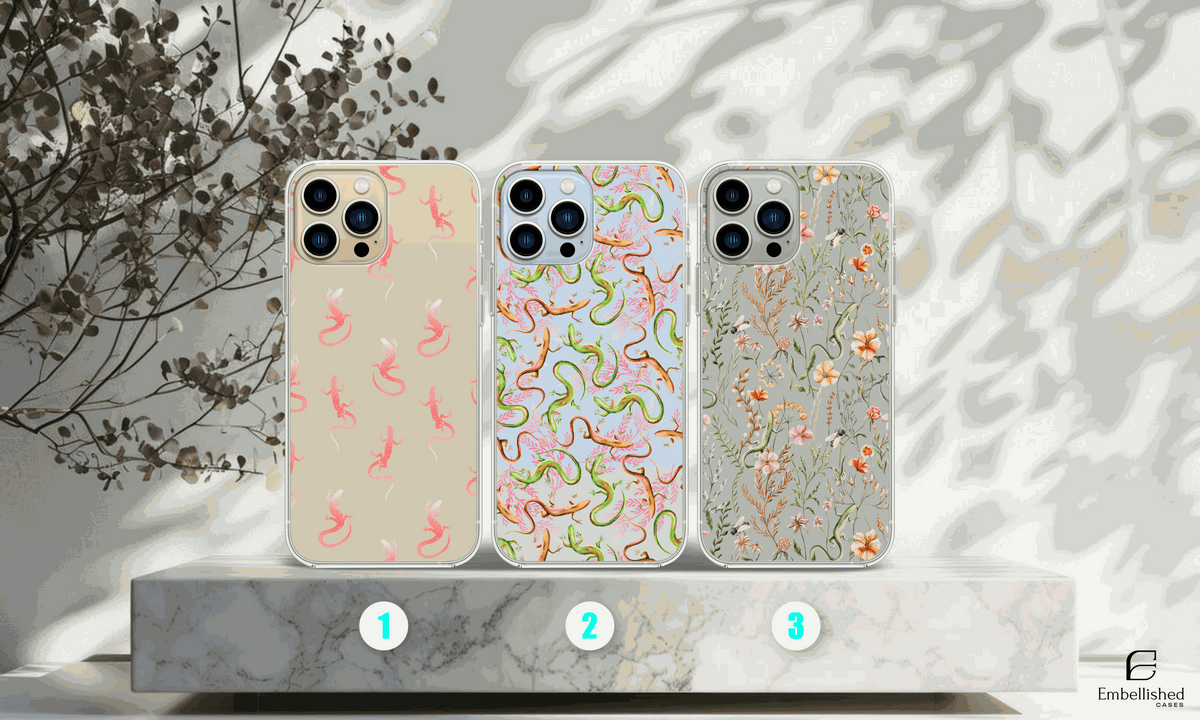 Clear phone cases with vibrant lizard and floral wild flower designs on a marble platform