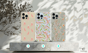 Clear phone cases with vibrant lizard and floral wild flower designs on a marble platform